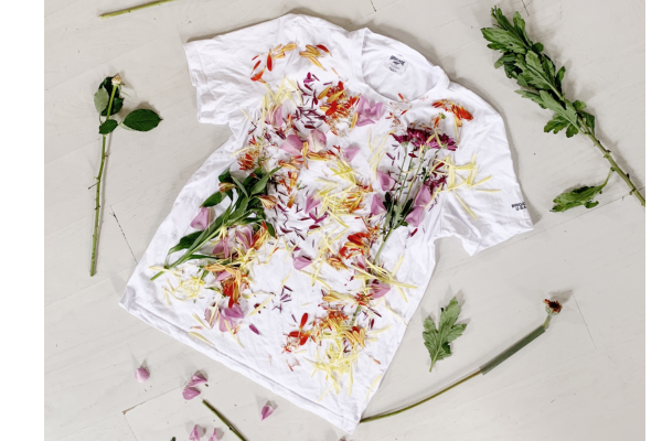 A DIY textiles project, s white organic cotton shirt with colorful flower designs created through natural dyeing techniques. The shirt features pink and green hues from the natural dyes used.