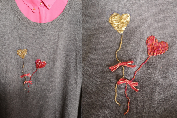 A grey pullover hand-embroidered with glass beads and ribbons, representing 2 baloons with a heart shape. One is red and the other one is golden.