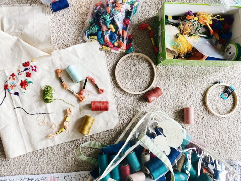 The table is surrounded by various DIY fashion supplies, including a sewing machine, sewing kits, fabrics, thread spools, scissors, and pins.